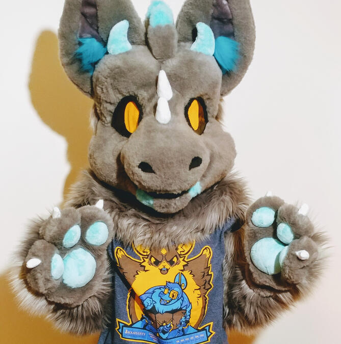 sky2 A person wearing the fursuit of Sky, a grey dutch angel dragon. They are standing with their paws raised slightly in front of them.