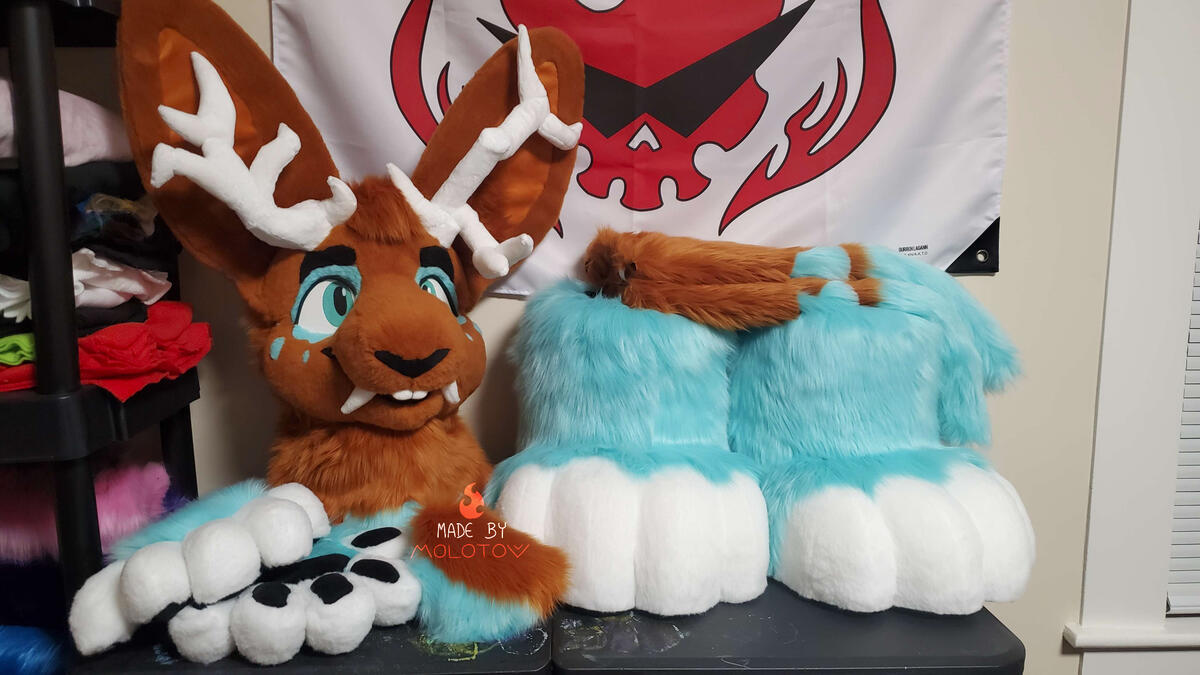 SIENNA1 The fursuit head, handpaws, feetpaws, tail, and arm sleeves of Sienna, a wolpertinger character. He has a passive expression, two asymmetrical antlers, and saber teeth.